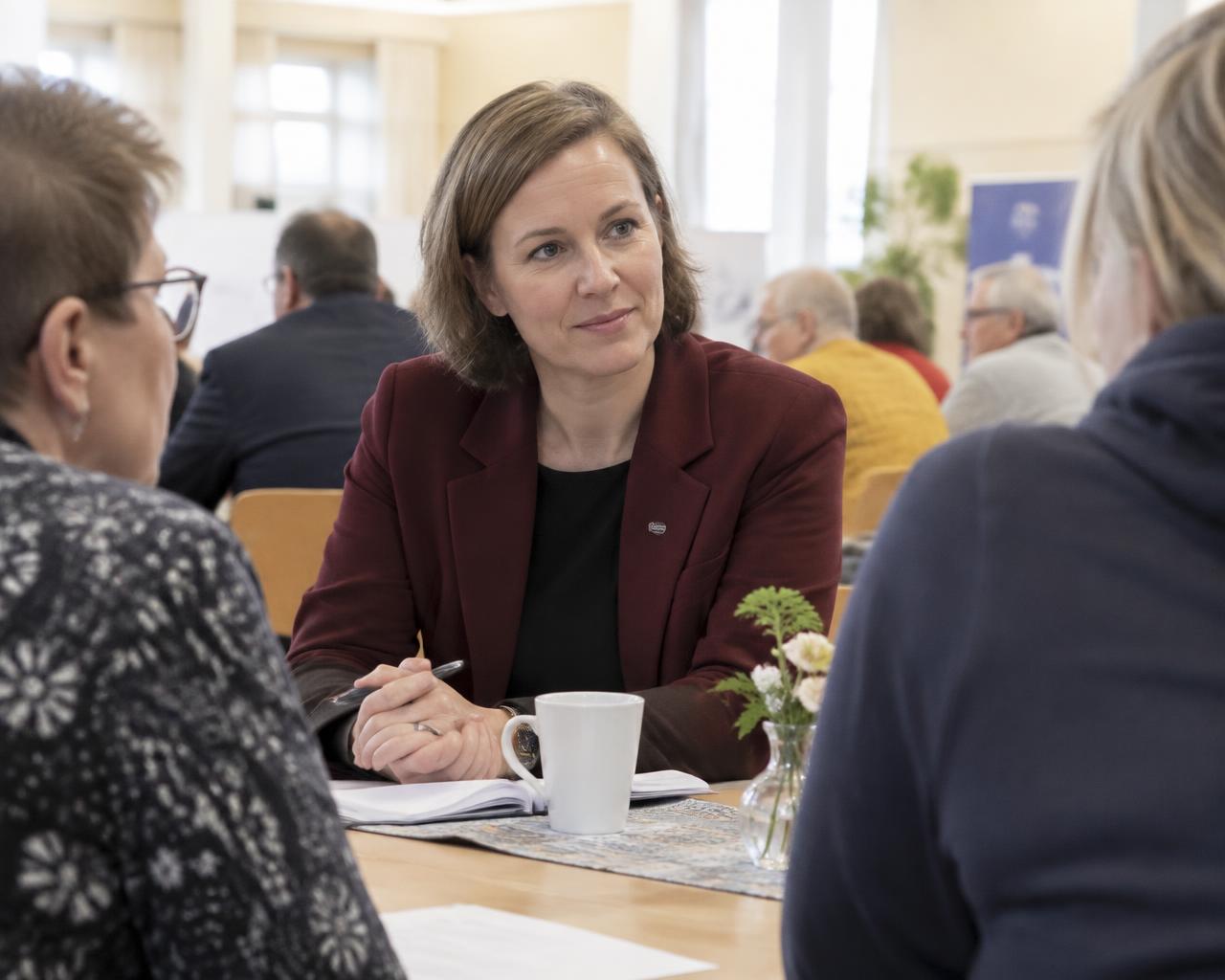 Anna Lahtinen keskustelee ihmisten kanssa valoisassa tilaisuudessa.